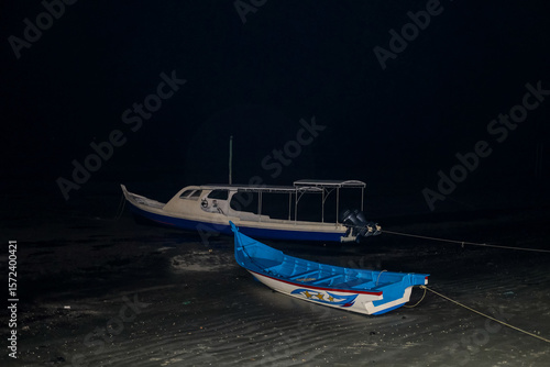 Wooden tourist boats rest on the wet sand under the night sky, stranded by the receding tide on a quiet, moonless coastal beach.