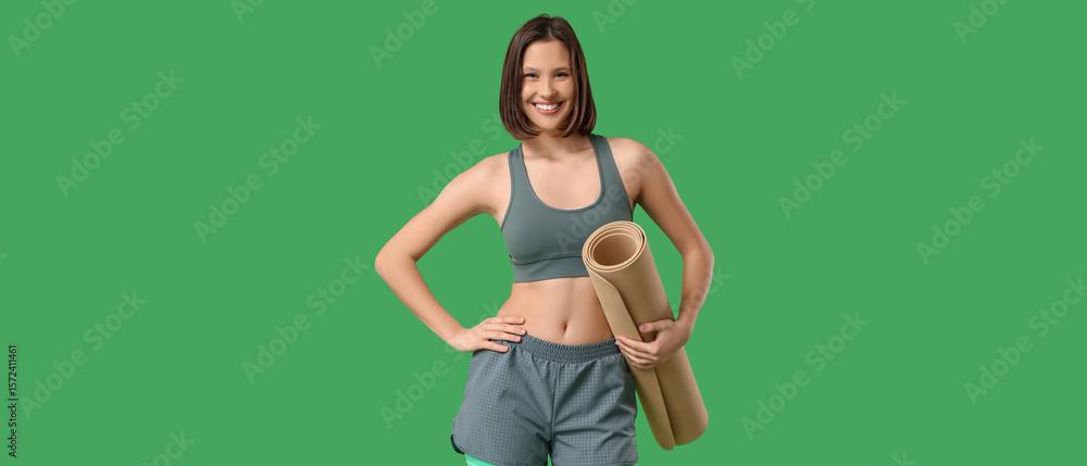 Fototapeta premium Sporty young woman with fitness mat on green background