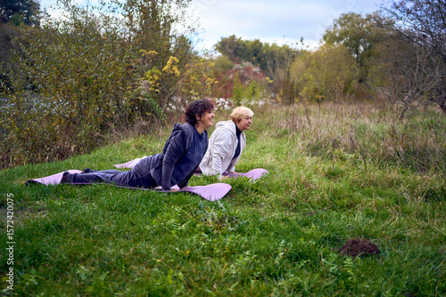 middle-aged woman teaches her old mother somatic exercises and yoga to maintain health by the river in autumn
