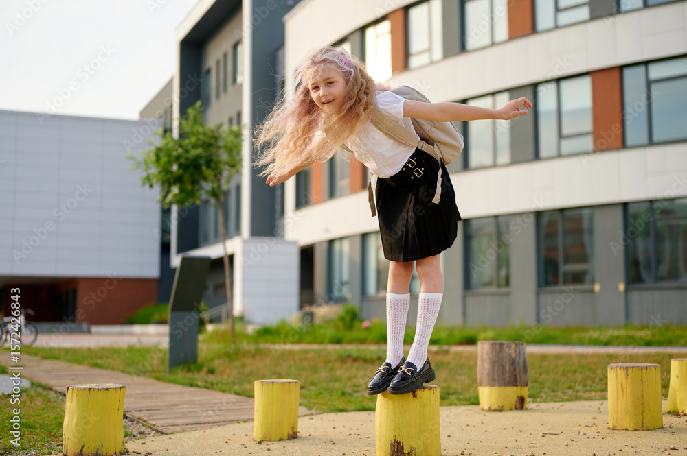 Obraz premium schoolgirl on playground balancing on wooden post, arms spread wide, springtime adventure. her playful pose reflects energy in modern schoolyard, carefree spirit of youth