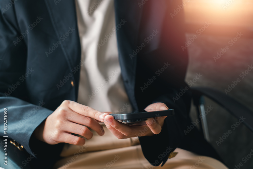 Obraz premium Close-up of a business professional using a smartphone in an office environment with warm sunlight.