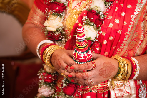 Close-up of Hands of Newly Married Indian Bengali Bride Holding Traditional Gachkouto in Red Banarasi Saree with Gold Jewelry and Floral Garland – Cultural Wedding Rituals of Bengal