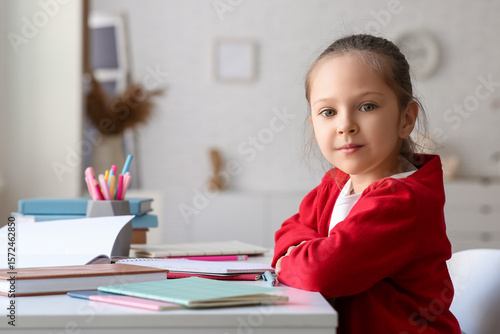 Cute little girl with books sitting by table and studying at home