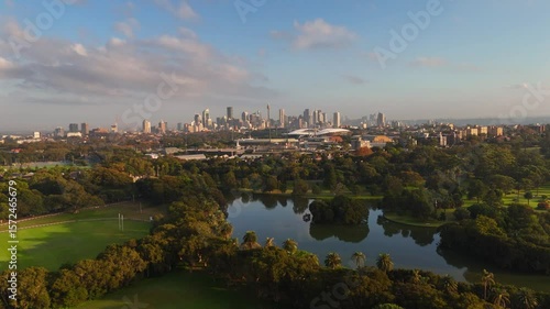 Aerial panoramic establishing of Centennial Park with skyline in background and lush trees under blue sky, Sydney NSW Australia