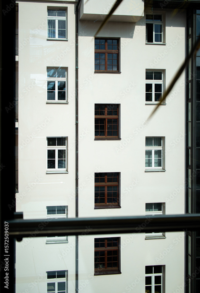 Naklejka premium A unique view of a building facade with numerous windows, seen through a glass pane which creates a subtle reflection of the same structure