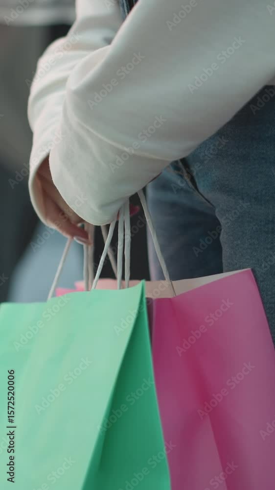 Side view of woman standing indoors holding mint and pink shopping bags, making hand movements around handles with polished nails, wearing casual white top and jeans, vibrant red and blue background Side view of woman standing indoors holding mint and pink shopping bags, making hand movements around handles with polished nails, wearing casual white top and jeans, vibrant red and blue background