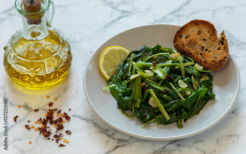 Fotografie Sauteed Chicory Greens - a traditional Italian side dish on a plate served with toasted bread and a slice of lemon