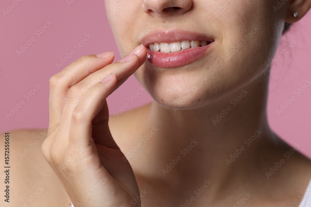 Obraz premium Young woman with lip balm on her lips against pink background, closeup