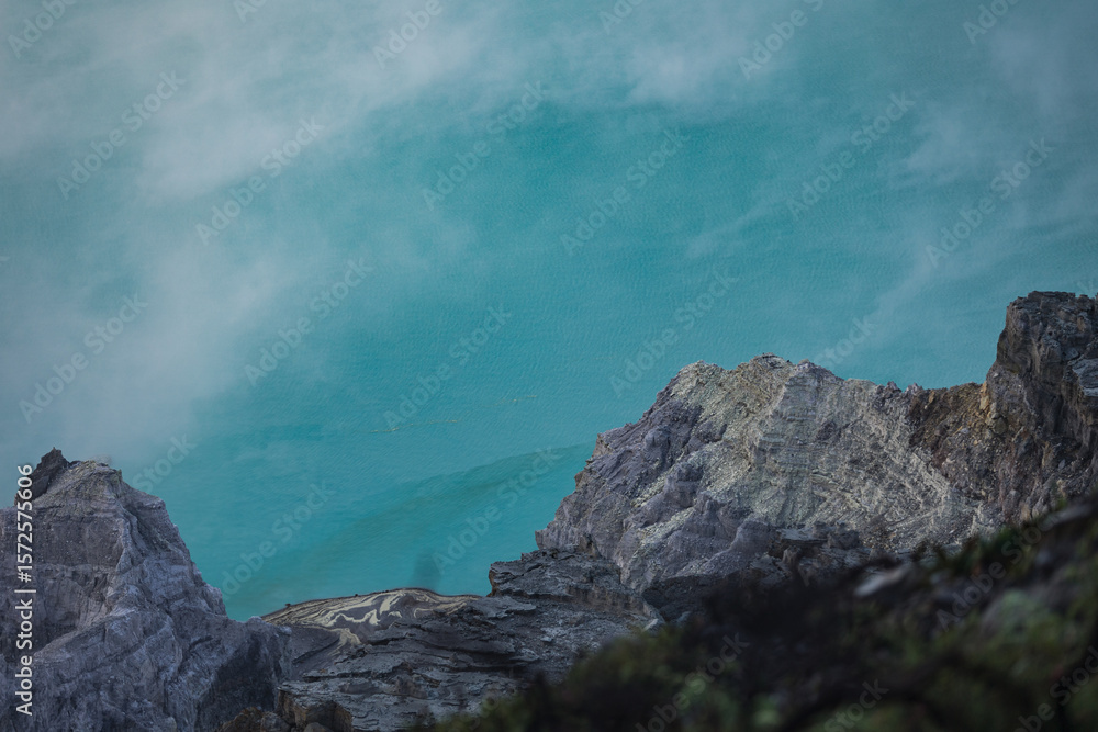View of jagged grey rocks cutting through a milky, ethereal turquoise sky, the scene exuding a surreal and otherworldly atmosphere, Ijen Volcano Crater, East Java, Indonesia. View of jagged grey rocks cutting through a milky, ethereal turquoise sky, the scene exuding a surreal and otherworldly atmosphere, Ijen Volcano Crater, East Java, Indonesia.