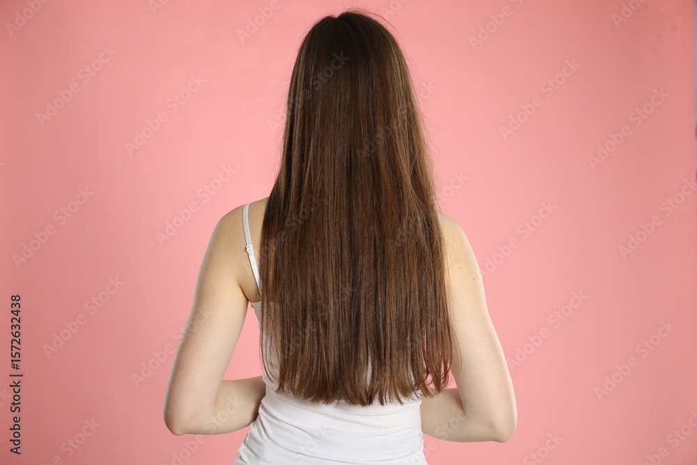 Woman with long hair on light pink background, back view Woman with long hair on light pink background, back view