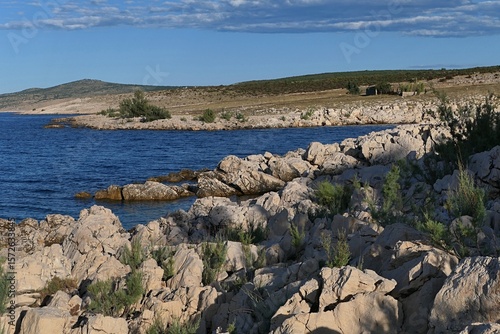 Summer landscape with rocky Croatian shoreline south of Razanac town, northern Dalmatia, Croatia. Bay water and arid foliage visible, blue skies in background. 