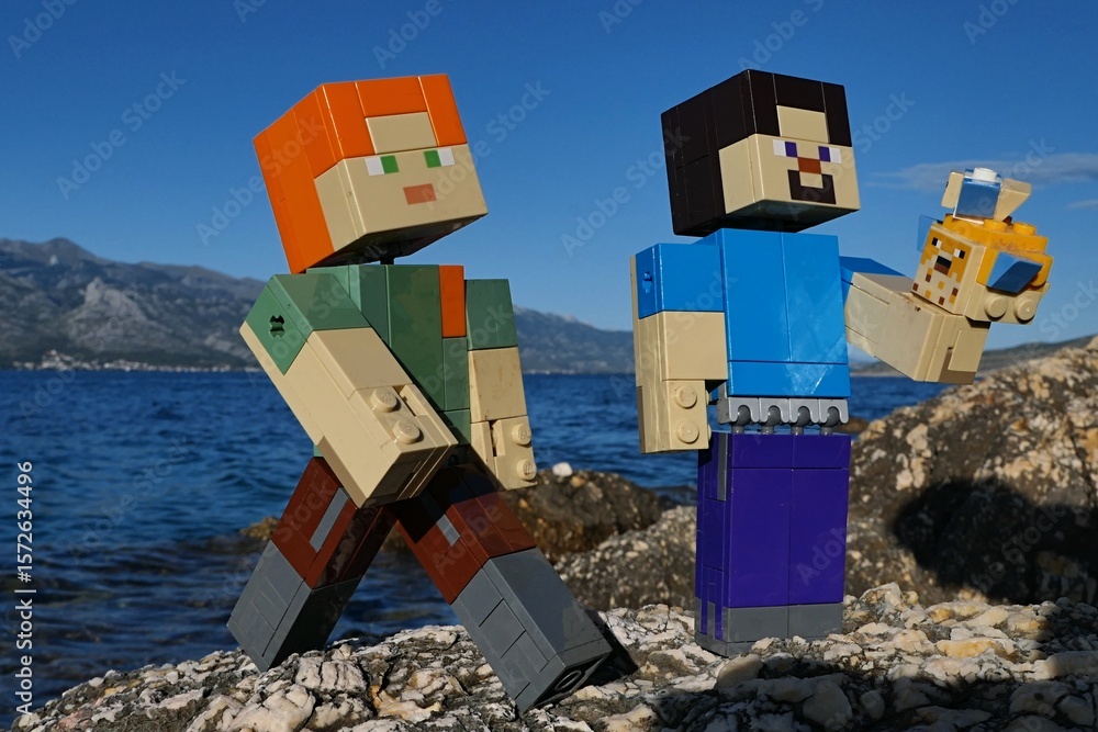 Naklejka premium LEGO Minecraft Steve examining LEGO Pufferfishes aquatic mobs, Alex walks next to him. Location rocky Croatian beach, bay water and Velebit mountain in background. Blue summer skies. 