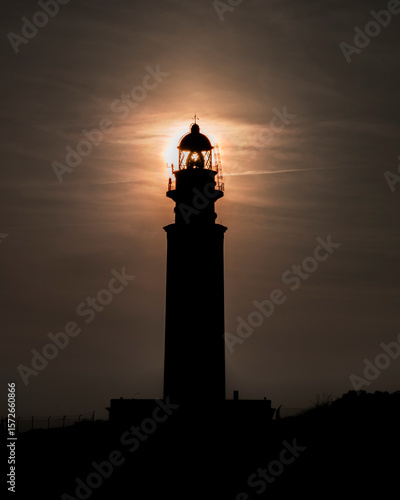 Stunning silhouette of a tall lighthouse against the sun.