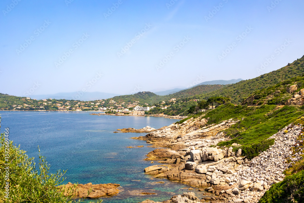 Fototapeta premium Rocky coastline with turquoise sea and green hills, Corsica, 13 June 2025