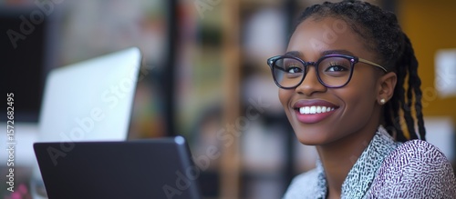 Young Woman With Glasses Smiling While Working on a Laptop in a Cozy Office Setting During the Afternoon