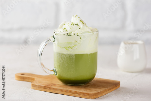 Cup of fresh green matcha latte tea with cream on wooden board