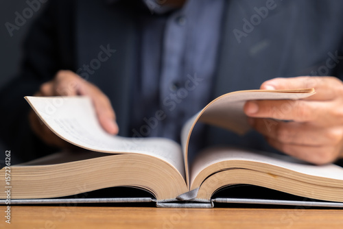 Foto Close-up of hands flipping pages of an open book on wooden desk, symbolizing res