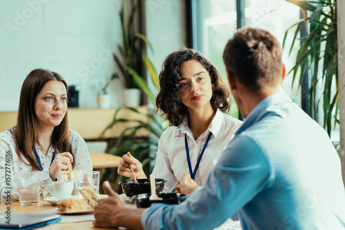 Three young coworkers chatting over healthy lunch in bright office cafeteria