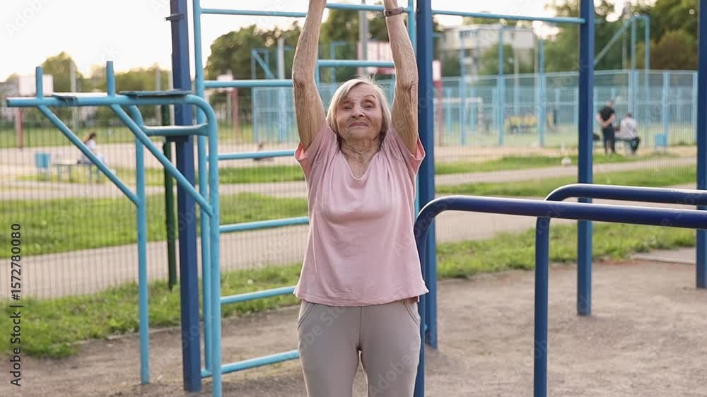 An elderly woman over 80 performs a breathing exercise outdoors. She raises her arms with a deep inhale and lowers them with exhale, showing balance and serenity. An elderly woman over 80 performs a breathing exercise outdoors. She raises her arms with a deep inhale and lowers them with exhale, showing balance and serenity.