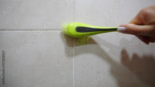 Woman scrubbing grout between tiles dirty and covered with black mold in bathroom, close-up. Fight against household mold, danger of mold to health, cleaning
