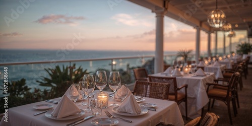 Elegant restaurant setting with ocean view at sunset featuring tables and chairs and place settings