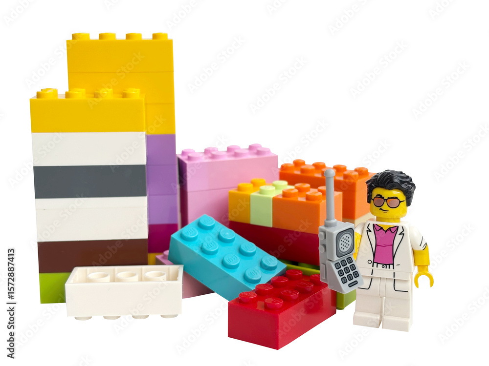 Naklejka premium A miniature Lego man: a businessman talking on a mobile phone, standing next to colorful bricks on a white background.