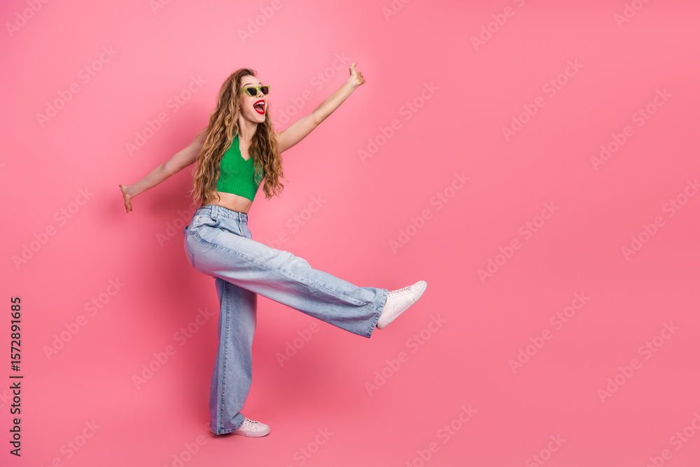 Fototapeta premium Cheerful young woman in vibrant green top and jeans having fun against pink background, expressing joy and energy