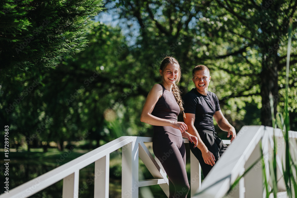 Fototapeta premium Smiling couple enjoy quality time outdoors, leaning on a wooden bridge in a lush green park, showcasing happiness and a strong connection. The bright day enhances the cheerful and relaxed atmosphere.