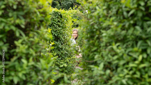A woman joyfully explores a vibrant green hedge maze on a sunny afternoon. Surrounding foliage creates a serene atmosphere as she navigates the intricate paths