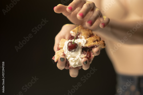This captivating image showcases a hand presenting a slice of pie, topped with cream and a cherry. The focus on color and texture creates a unique visual appeal that entices viewers.