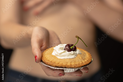 A focus on hands holding a delightful pie featuring whipped cream and a cherry, presenting a warm invitation to taste something sweet amidst an elegant, dark background.