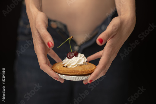 A close-up of hands holding a charming pie with whipped cream and a cherry on top, showcasing delicious dessert aesthetics in a playful and elegant manner against a dark backdrop.