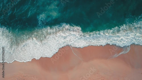 Turquoise waves kissing pink shoreline. Crashing turquoise ocean waves meet pristine sandy beach, forming mesmerizing natural scene captured from aerial perspective, showcasing beauty of coastline