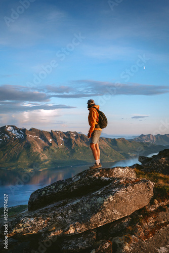Man hiking solo in Norway standing on cliff above fjord active travel adventure lifestyle, tourist walking alone in mountains summer vacations backpacking trip in the wild
