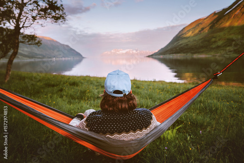 Man relaxing alone in hammock travel lifestyle summer vacations outdoor in Norway, traveler enjoying calm sunset view of mountains and fjord harmony and freedom eco tourism camping trip