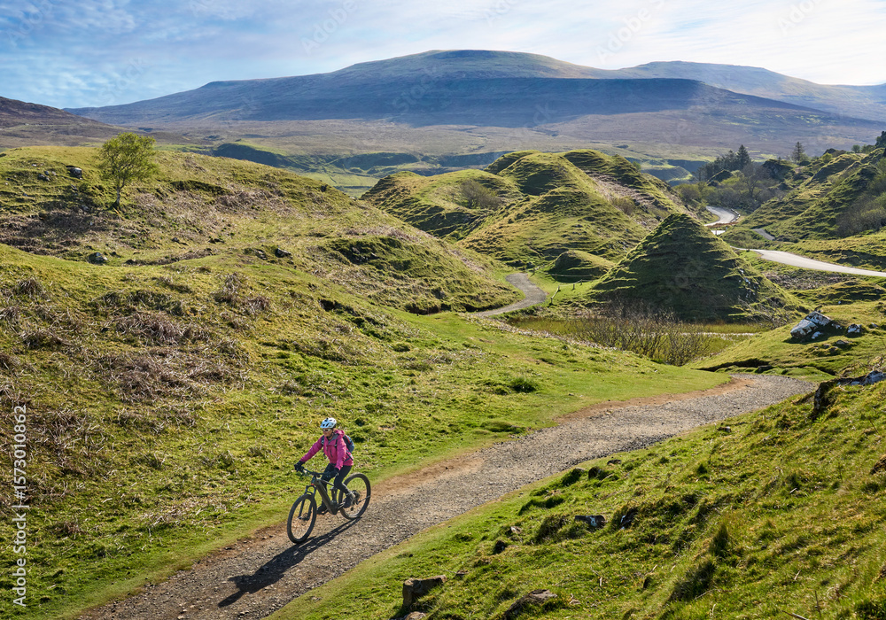 Fototapeta premium active woman riding her electric mountain bike in the spectacular volcabinic landscape of Glen Fairy on the Isle of Skye in Scotland, UK