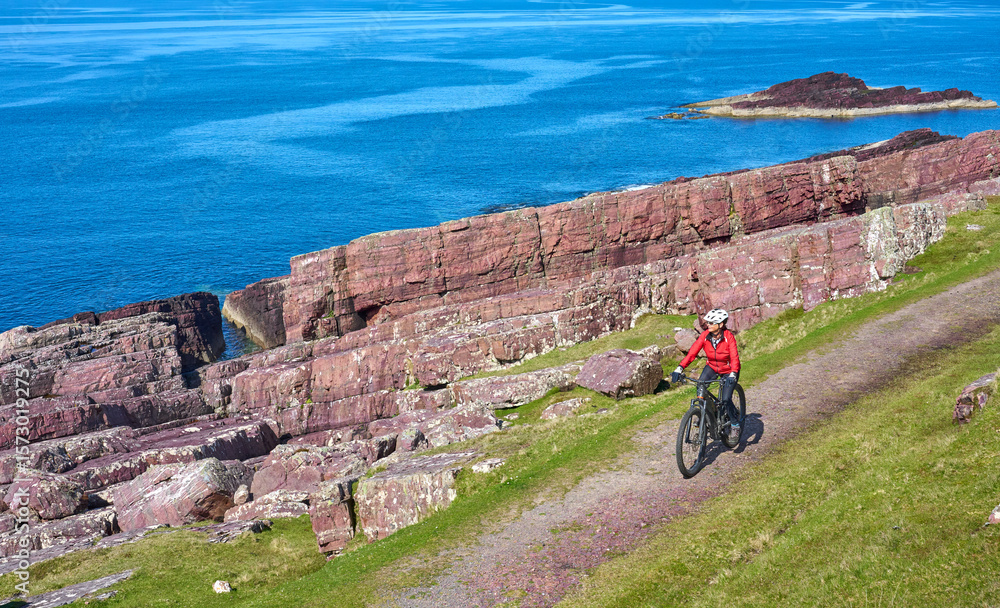 Fototapeta premium active senior woman riding her electric mountain bike on the cliffs near Rua Reidh Lighthouse next to Gairloch in north western Scotland, UK