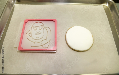 Slika na platnu A sugar cookie with white royal icing and a stencil holder with a buzz lightyear stencil for airbrushing with food color
