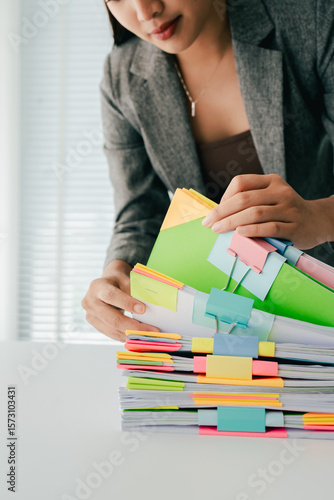 Young female employee is working with a pile of documents to search for information and check documents on the table. Document search concept.
