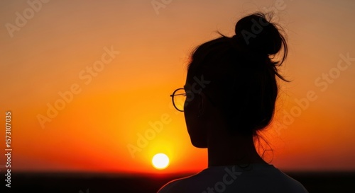 Silhouette of a person with glasses looking at the bright orange sunset