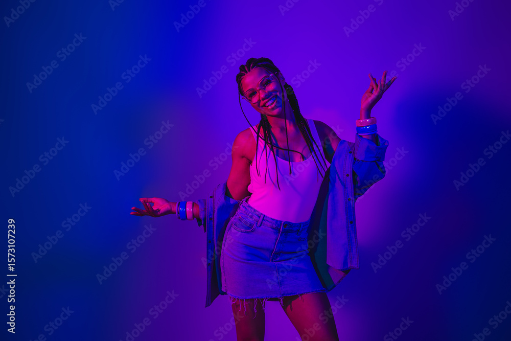 Obraz premium Stylish young woman in neon lighting shows positive gestures wearing modern casual denim fashion for nightlife