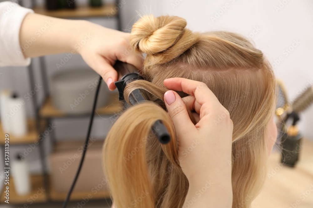 Fototapeta premium Hairdresser curling woman's hair in salon, closeup