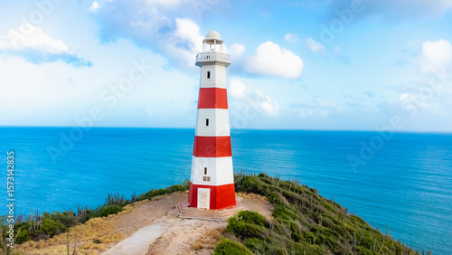 Red and white lighthouse is on a rocky cliff overlooking the ocean