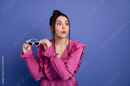 Fotografía Fashionable young woman in pink ruffled dress holding stylish sunglass, expressi