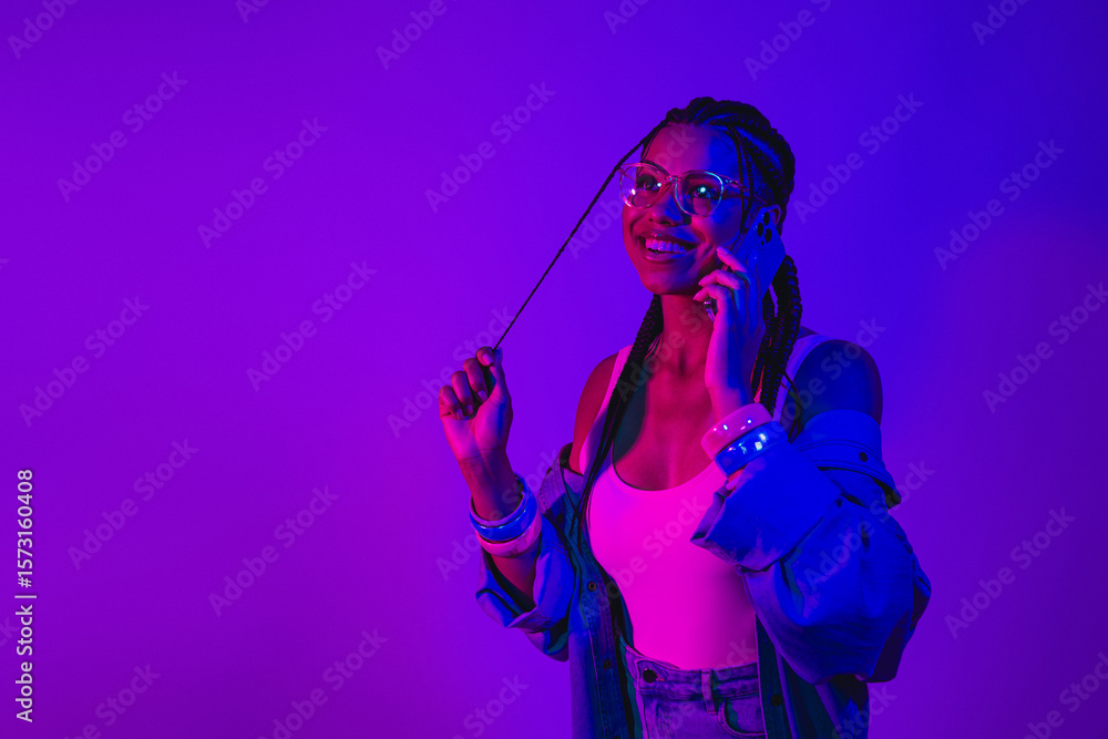 Naklejka premium Young woman in neon lighting enjoying a phone call wearing denim jacket
