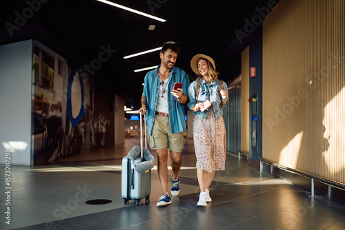 Foto Happy couple using mobile phone while walking through departure terminal at station