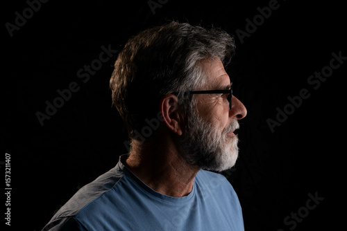 Photos Mature handsome man with beard side profile portrait in chiaroscuro style on black background, mysterious and dramatic mood