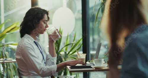 Young woman drinking water while typing on laptop during office break in bright cafe
