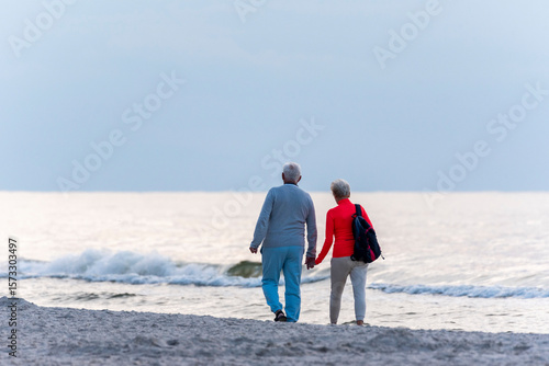Fototapeta Naklejka Na Ścianę i Meble -  Elderly couple walking hand in hand on a sandy beach near the Baltic Sea. 
