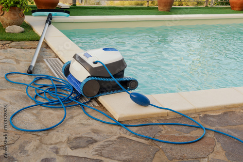 At the pool with clean turquoise water, there is a cleaning robot and a pool cleaning brush. The concept of cleaning pools in hotels, resorts and country houses.